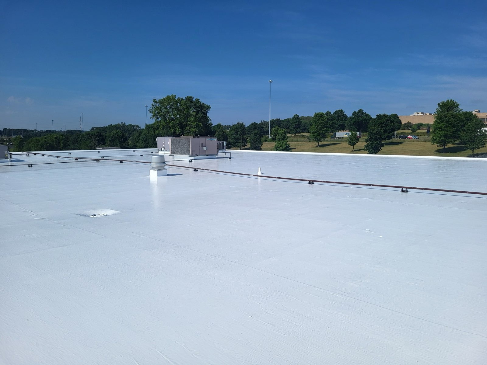 Wide view of a freshly coated white commercial roof under clear blue sky